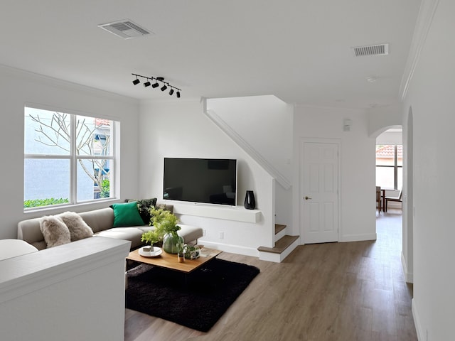 living area with arched walkways, visible vents, crown molding, and stairway