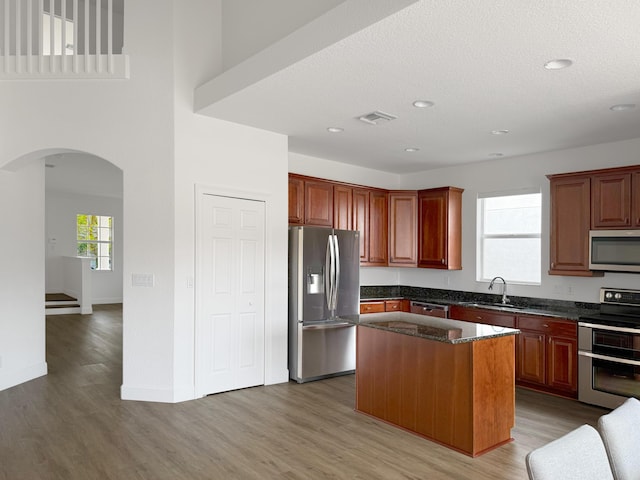 kitchen featuring arched walkways, a sink, visible vents, appliances with stainless steel finishes, and a center island