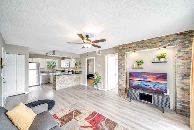 living area with visible vents, light wood-style floors, ceiling fan, and a textured ceiling