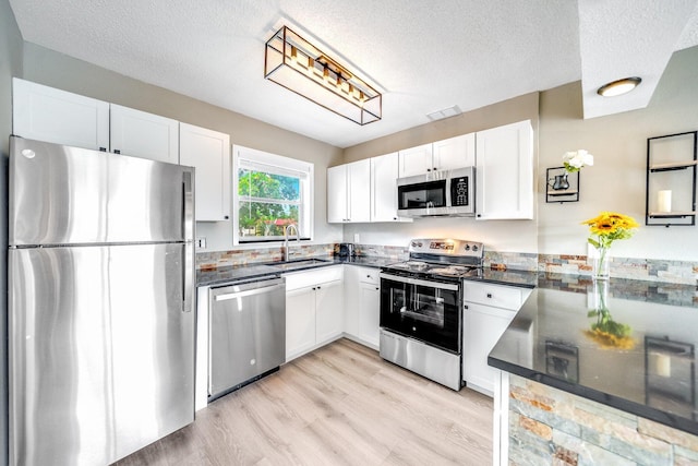 kitchen featuring dark countertops, white cabinetry, stainless steel appliances, and a sink