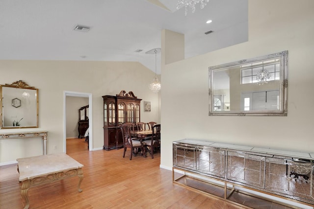 hall with lofted ceiling, light wood-style floors, baseboards, and a chandelier