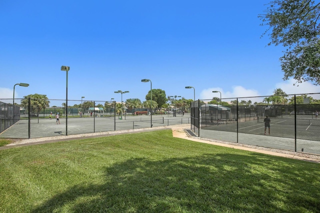 view of tennis court featuring a lawn and fence