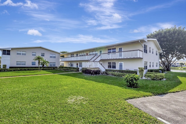 rear view of house featuring a lawn, a balcony, and stucco siding