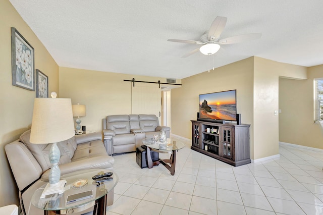 living room featuring light tile patterned floors, a barn door, baseboards, a ceiling fan, and a textured ceiling