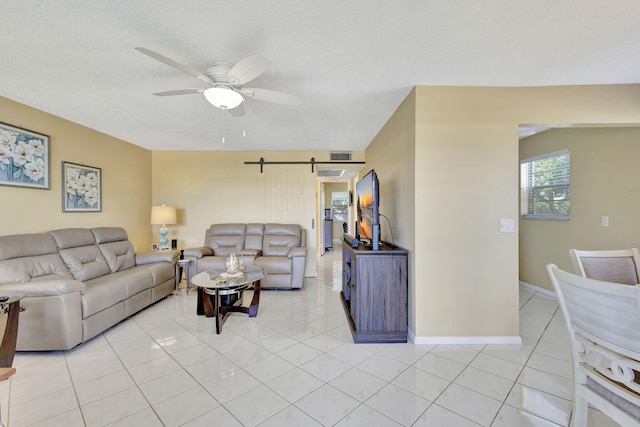 living area featuring light tile patterned floors, visible vents, a barn door, a ceiling fan, and a textured ceiling