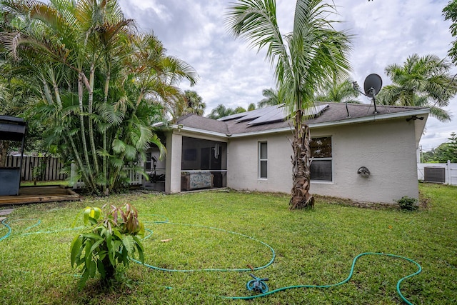 rear view of house with solar panels, fence, a sunroom, a lawn, and stucco siding