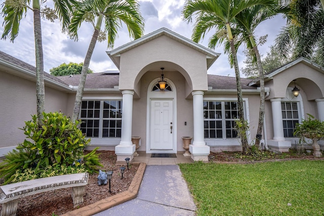 entrance to property with a yard, roof with shingles, and stucco siding