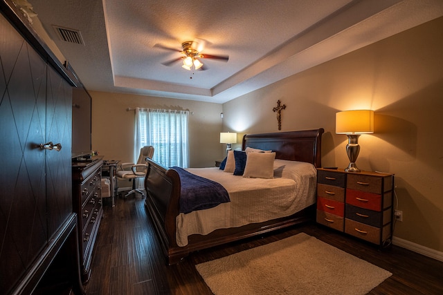 bedroom with dark wood-type flooring, a tray ceiling, visible vents, and baseboards