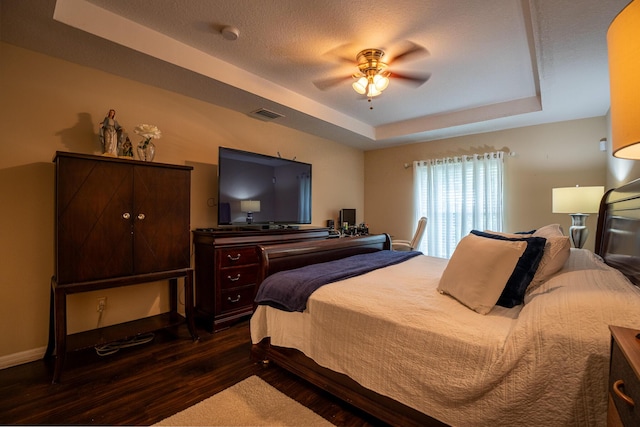 bedroom with visible vents, ceiling fan, dark wood-style flooring, a tray ceiling, and a textured ceiling