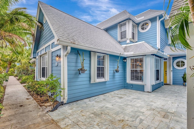 view of side of home featuring a shingled roof and a patio area