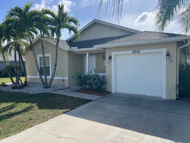 single story home with an attached garage, driveway, a front lawn, and stucco siding