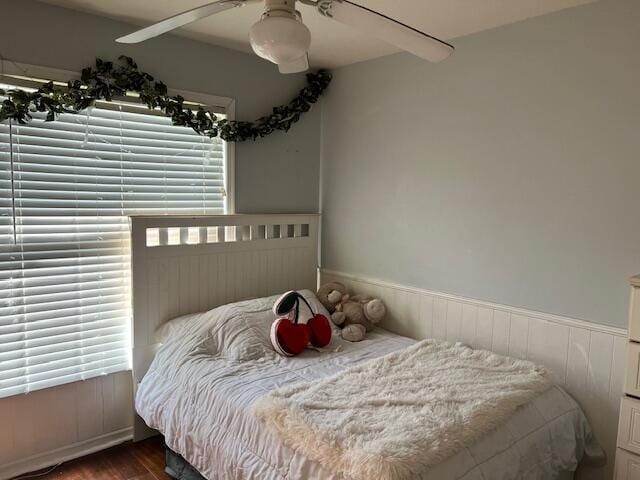 bedroom with a wainscoted wall, a ceiling fan, and dark wood-style flooring