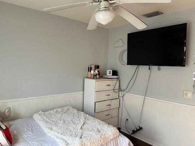 bedroom featuring ceiling fan, wainscoting, and visible vents