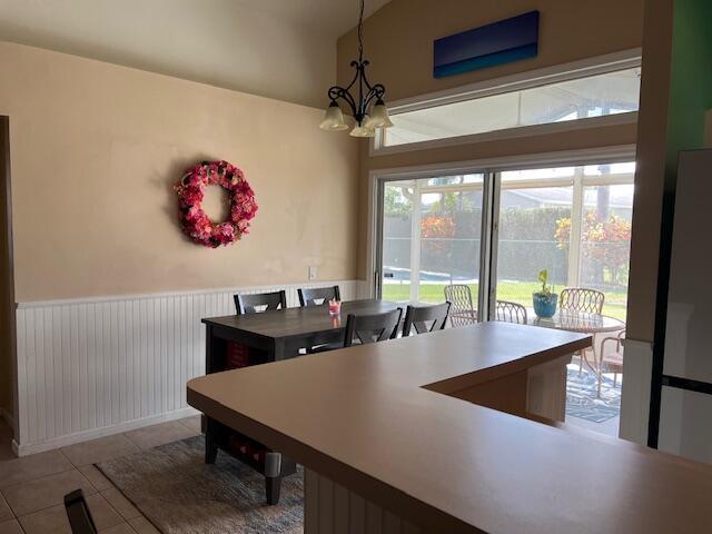 dining room featuring a wainscoted wall, vaulted ceiling, a notable chandelier, and tile patterned floors