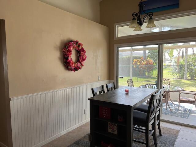 dining space with a wainscoted wall, an inviting chandelier, and tile patterned floors