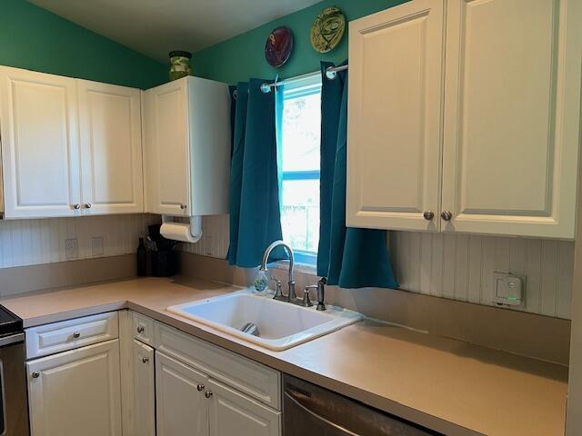 kitchen featuring black dishwasher, white cabinets, a sink, and light countertops