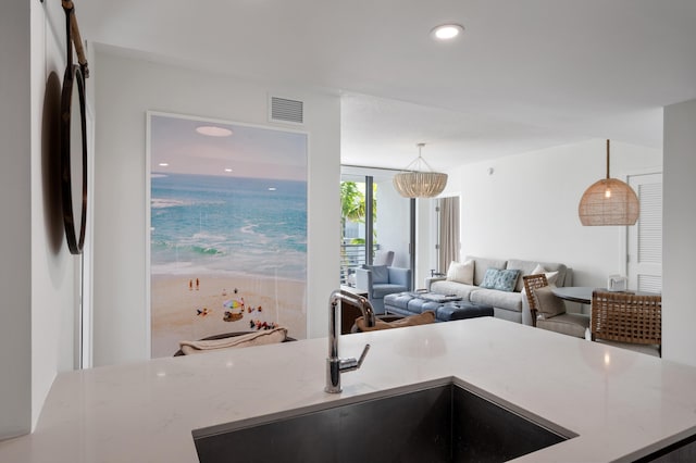 kitchen with pendant lighting, visible vents, open floor plan, a sink, and light stone countertops