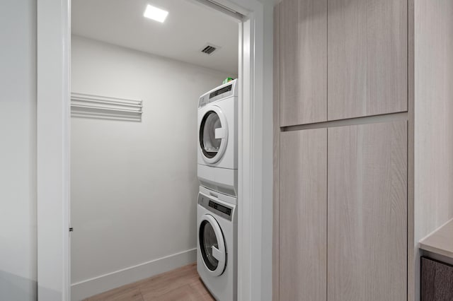 laundry room featuring laundry area, baseboards, visible vents, stacked washer and clothes dryer, and light wood-type flooring