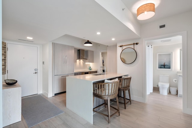 kitchen featuring visible vents, a kitchen breakfast bar, light countertops, wall chimney exhaust hood, and modern cabinets