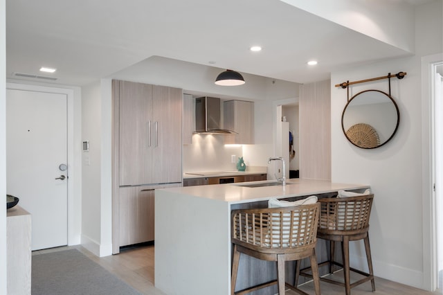 kitchen with light wood-style floors, modern cabinets, wall chimney range hood, a kitchen bar, and a sink