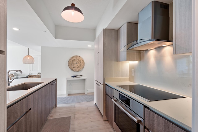 kitchen featuring a sink, stainless steel oven, modern cabinets, wall chimney exhaust hood, and black electric cooktop