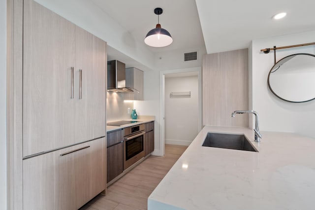 kitchen with wall chimney exhaust hood, modern cabinets, light wood-style flooring, oven, and a sink