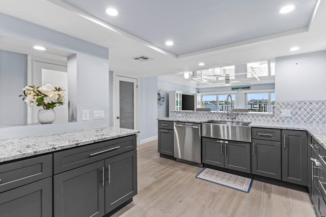 kitchen with visible vents, dishwasher, light wood-style flooring, a tray ceiling, and a sink