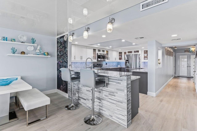 kitchen with visible vents, glass insert cabinets, appliances with stainless steel finishes, light stone countertops, and white cabinetry