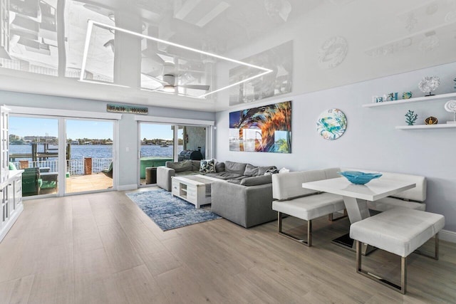 living room with a water view, light wood-style floors, a towering ceiling, and baseboards