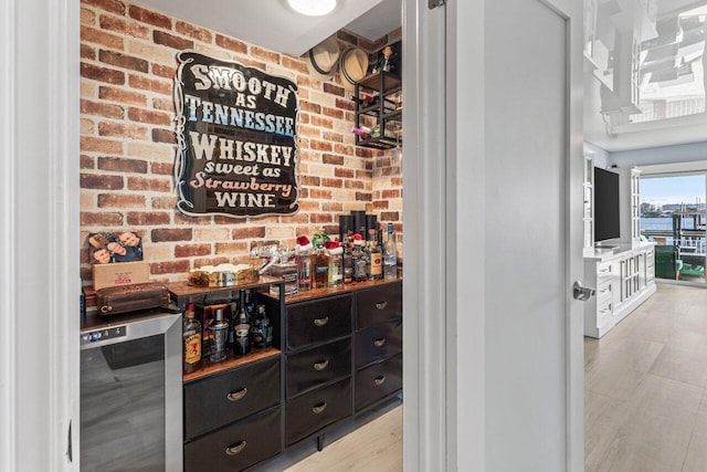 bar with light wood finished floors, brick wall, and wine cooler