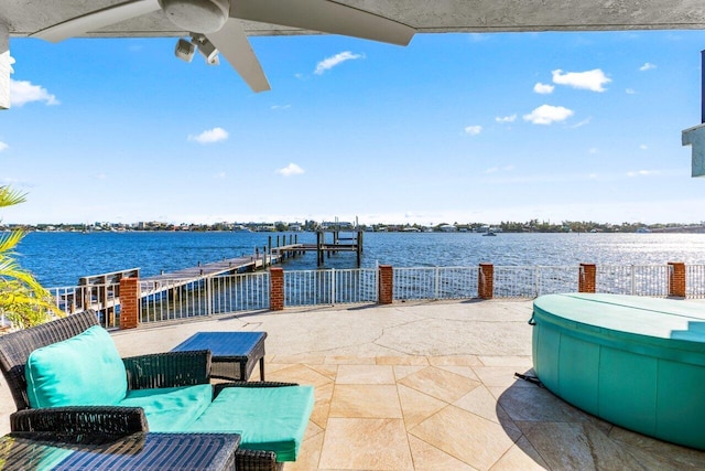 view of patio featuring ceiling fan, a boat dock, a water view, and fence