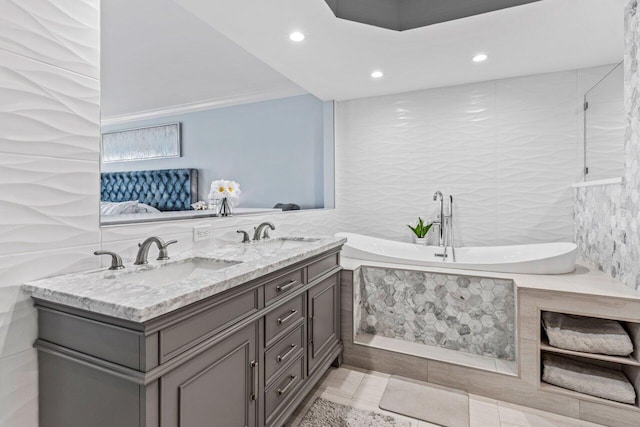 full bathroom with a sink, tile walls, a tub with marble appearance, and double vanity