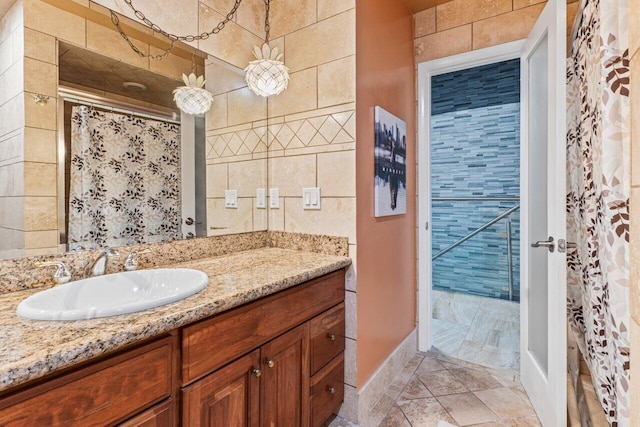 bathroom with tile walls, a shower with shower curtain, vanity, and baseboards