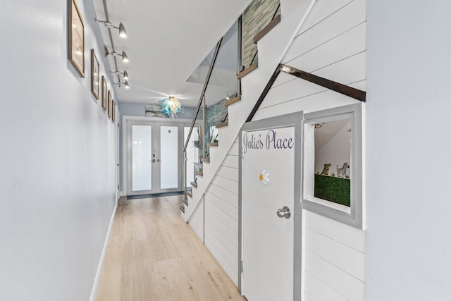 hall featuring light wood-type flooring, french doors, baseboards, and stairs