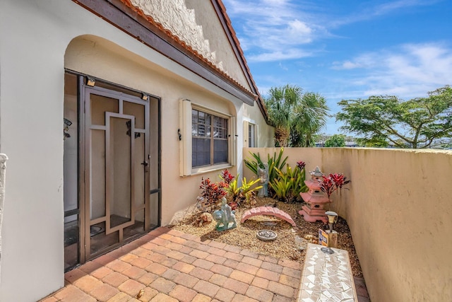 view of exterior entry featuring a tile roof, fence, and stucco siding