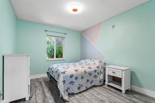 bedroom featuring light wood-type flooring, a textured ceiling, and baseboards