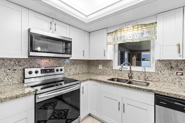 kitchen featuring white cabinets, light stone counters, stainless steel appliances, and a sink