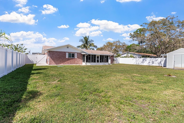 rear view of property featuring brick siding, a lawn, a fenced backyard, and a sunroom