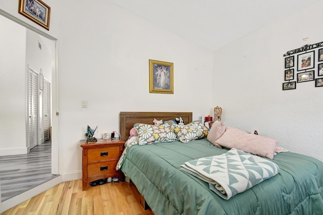 bedroom with vaulted ceiling, wood finished floors, and baseboards