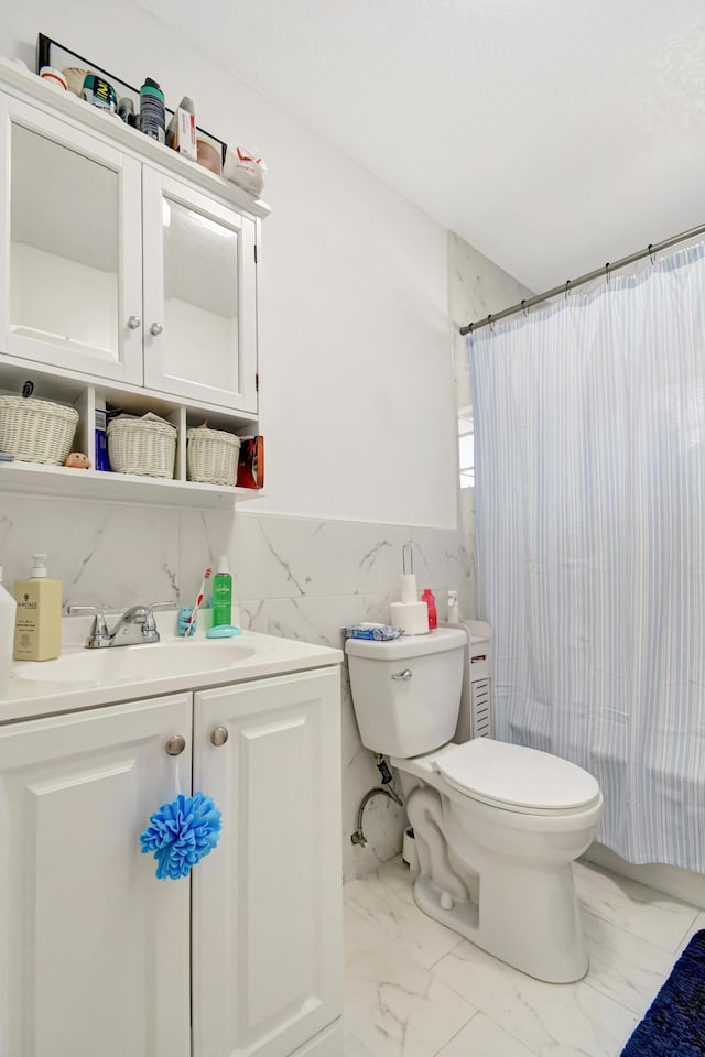 full bathroom with wainscoting, toilet, marble finish floor, vanity, and tile walls