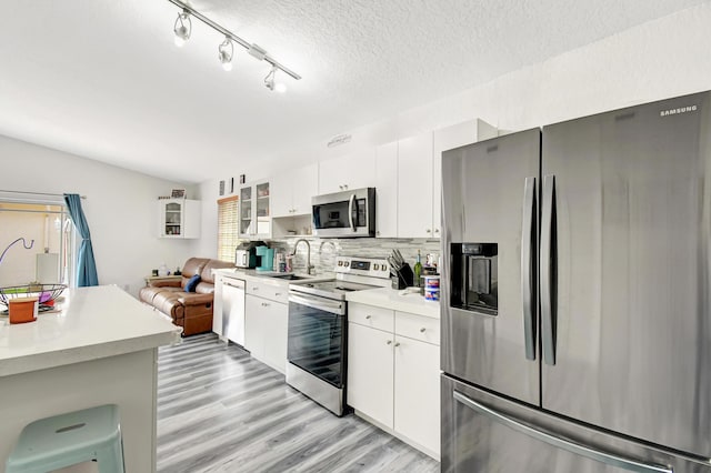 kitchen featuring white cabinets, appliances with stainless steel finishes, glass insert cabinets, light countertops, and a sink