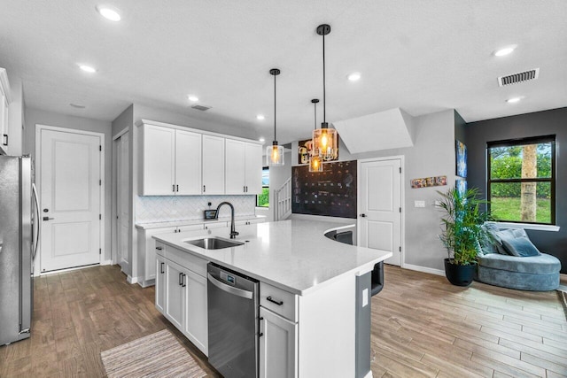 kitchen featuring white cabinets, an island with sink, appliances with stainless steel finishes, light countertops, and a sink