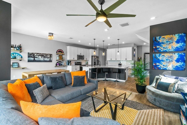 living room featuring light wood-style flooring, visible vents, a ceiling fan, and recessed lighting