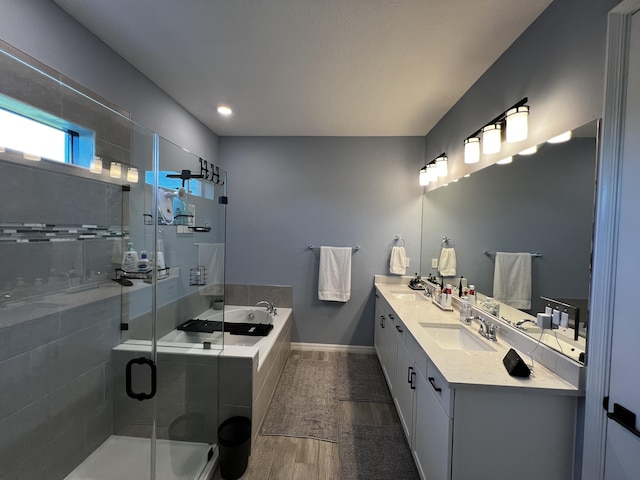 full bathroom with double vanity, a shower stall, a sink, and wood finished floors