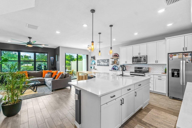 kitchen featuring a kitchen island with sink, white cabinetry, stainless steel appliances, and light countertops