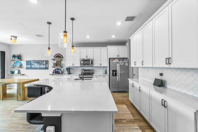 kitchen with decorative light fixtures, appliances with stainless steel finishes, white cabinetry, light stone countertops, and a large island with sink