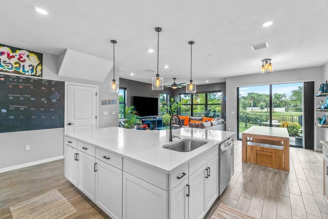 kitchen with white cabinets, dishwasher, a kitchen island with sink, light countertops, and a sink