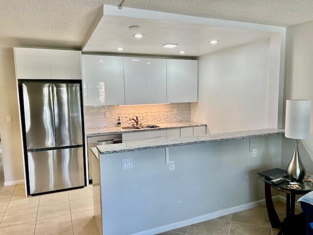 kitchen featuring stainless steel appliances, a peninsula, light stone countertops, and white cabinets