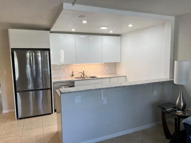 kitchen with a peninsula, a sink, white cabinets, appliances with stainless steel finishes, and modern cabinets