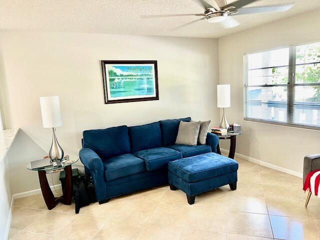 living room with a textured ceiling, ceiling fan, light tile patterned floors, and baseboards